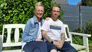 Eine Frau und ein Mann sitzen auf einer weißen Bank und lächeln in die Kamera. © NDR Foto: Astrid Wulf