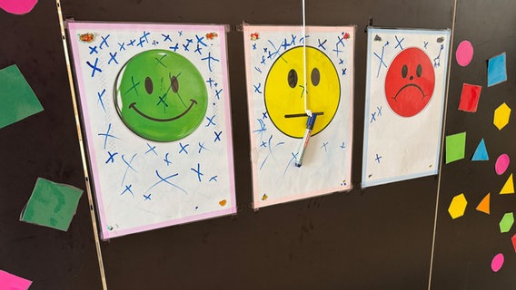 Zettel mit einem grünen, gelben und roten Smiley hängen an einer Wand in der Mensa der Grundschule Oststeinbek und können mit einem Stift angekreuzt werden. Zettel mit einem grünen, gelben und roten Smiley hängen an einer Wand in der Mensa der Grundschule Oststeinbek und können mit einem Stift angekreuzt werden. © NDR Foto: Daniela Tabarelli
