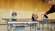 Eine Gruppe Menschen spielt Tischtennis in einer Sporthalle. © NDR Foto: Lisa Pandelaki