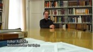 Der Medizinhistoriker Volker Roelcke an einem langen Tisch vor einem Bücherregal. © NDR 