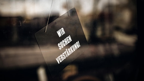 Eine Schild mit der Aufschrift "Wir suchen Verstärkung" hängt in einem Fenster. © picture alliance Foto: Michael Bihlmayer