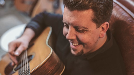 Peter Widereck lachend mit einer Akustikgitarre. © Promo 