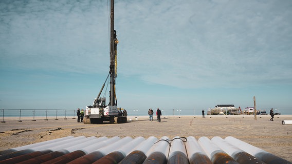 Rohre liegen am Strand von St. Peter-Ording neben einem Kran. © TZ SPO 