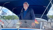 Friedrich Genthe steht am Steuerrad seines Motorboots "Dschensy". © NDR Foto: Gerrit Hoss