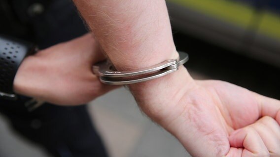 Ein Polizist sichert Hand eines Mannes mit Handschellen vor einem Streifenwagen. © NDR Foto: Pavel Stoyan