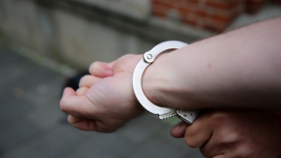 Ein Polizist sichert Hand eines Mannes mit Handschellen. © NDR Foto: Pavel Stoyan