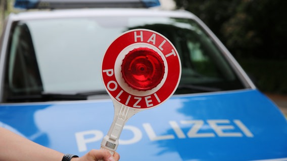 Ein Polizist hält eine Polizeikelle vor einem Streifenwagen. © NDR Foto: Pavel Stoyan