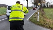 Ein Beamter der Polizei verfolgt mit einem Lasermessgerät einige Fahrzeuge auf einer Landstraße. © Imago Foto: Fotostand