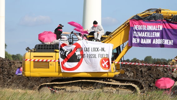 Mehrere Demonstrierende sitzen auf einem Bagger und haben diesen mit Transparenten behängt. © Westküsten-News Foto: Florian Sprenger