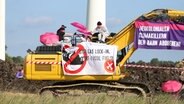 Mehrere Demonstrierende sitzen auf einem Bagger und haben diesen mit Transparenten behängt. © Westküsten-News Foto: Florian Sprenger