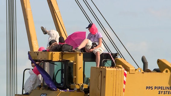Demonstrierende sitzen auf einem Bagger. © NDR Foto: NDR Screenshots