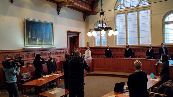 In einem Saal des Flensburger Landgerichts erheben sich ein Angeklagter in einem schwarzen Kapuzenpulli, Verteidigung, Staatsanwälte und Richter zur Eröffnung eines Missbrauchsprozesses © NDR Foto: Peer-Axel Kroeske