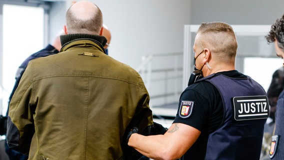 Ein Polizeibeamter führt den Angeklagten in den Sitzungssaal. © Frank Molter/dpa Foto: Frank Molter/dpa