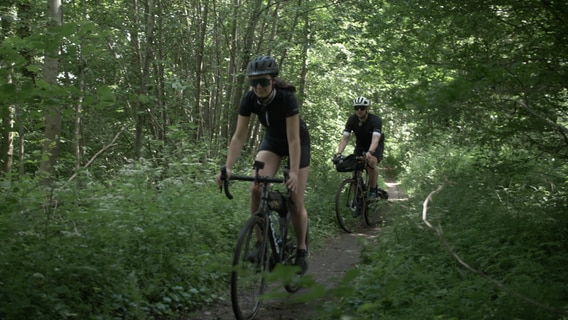 Zwei Radfahrer fahren auf einem nicht befestigten Weg durch den Wald. © NDR Foto: Dominik Dührsen