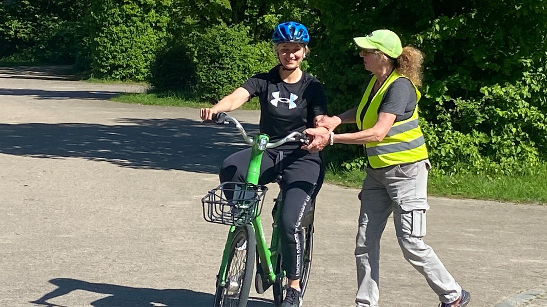 Eine Trainerin unterstüzt eine junge Frau beim Radfahrkurs.