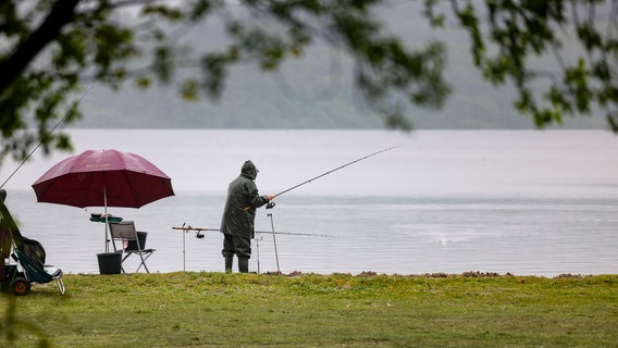 Ein Angler steht bei starkem Regen an einem See. © Frank Molter / dpa Foto: Frank Molter