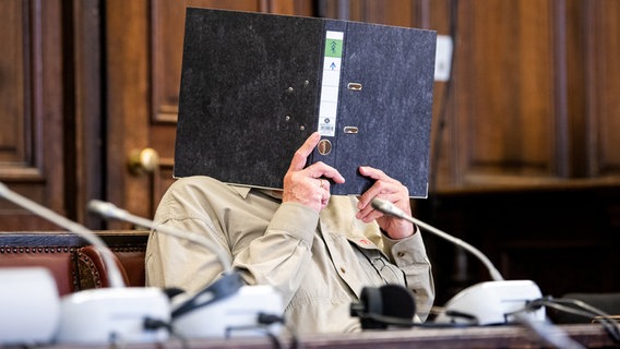 Ein Mann in einem Gerichtssaal verdeckt sein Gesicht mit einem Ordner © dpa-Bildfunk Foto: Daniel Bockwoldt