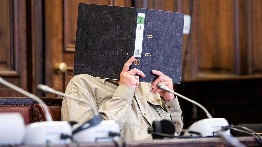 Ein Mann in einem Gerichtssaal verdeckt sein Gesicht mit einem Ordner