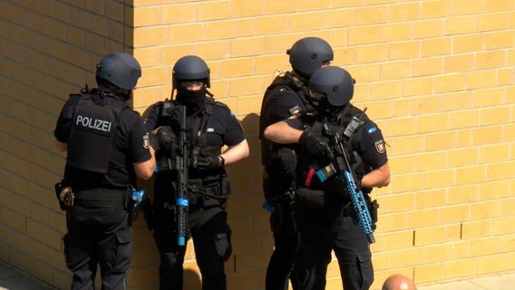 Im Zuge einer Amoklaufübung an einer Schule stehen 4 bewaffnete Einsatzkräfte der Polizei an einer Hauswand © NDR Foto: NDR Screenshots