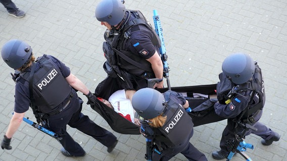 Einsatzkräfte der Polizei bringen eine verletzte Person mithilfe eines Tuches aus einem Gebäude © NDR Foto: NDR Screenshots