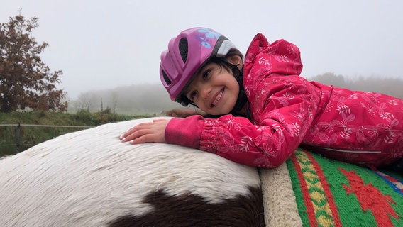 Ein junges Mädchen liegt auf dem Rücken von einem Pferd. © NDR Foto: Birte Steuer