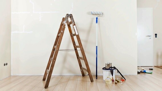 Eine Leiter, eine Farbrolle und Streichzubehör stehen vor einer hellen Wand einer Wohnung. © Imago Images Foto: Shotshop