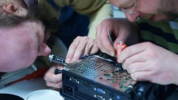 Zwei Männer reparieren einen Beamer.  © NDR Foto: Lisa Pandelaki