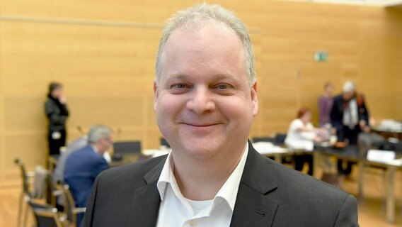 Kai Dolgner, Landtagsabgeordneter der SPD, steht vor einer Sitzung im Landtag Kiel vor der Kamera und lächelt. © Picture Alliance Foto: Carsten Rehder