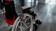 Eine Person in einem Rollstuhl rollt über einen Flur. © Imago Images/Westend61 