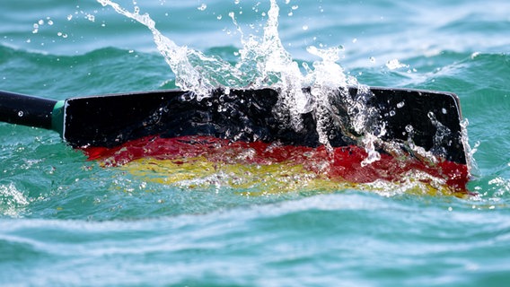 Ein Ruderblatt mit den de Farben taucht ins Wasser. Ein Ruderblatt mit den de Farben taucht ins Wasser. © picture alliance/dpa | Sven Hoppe Foto: Sven Hoppe