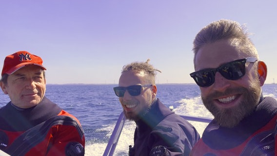 Drei Männer in Tauchausrüstung auf einem Motorboot auf dem Meer. © NDR Foto: NDR
