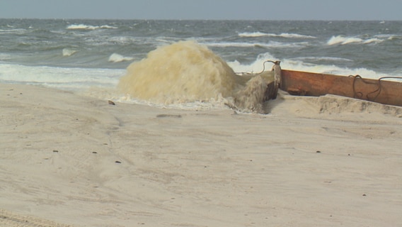 Ein Rohr spült ein Sand-Wasser-Gemisch auf einen Strand. © NDR 