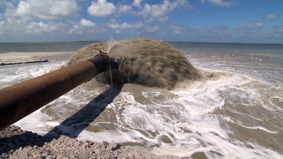 Eine Sand-Wasser-Masse kommt auf einem Rohr auf den Strand von Föhr vorgespült. © NDR 