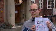 Lennart Saß hält ein Dokument in die Kamera mit der Beteiligung einer Petition. © NDR 