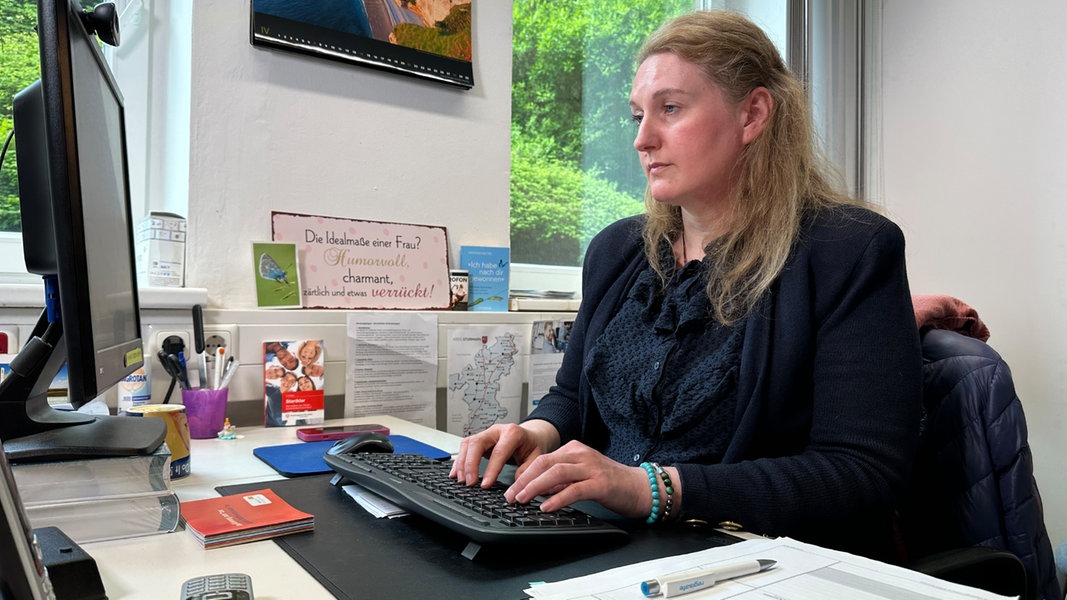 Eine Frau sitzt in einem Büro an einem Arbeitstisch und blickt auf den PC-Monitor.