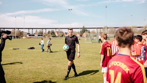 Schiedsrichter Pascal Martin tritt mit einem Ball in der Hand vor die beiden Jugendfußballmannschaften. © NDR Foto: Lisa Pandelaki