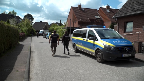 Zwei Polizisten gehen an einem Einsatzfahrzeug im Kieler Stadteil Dänischenhagen vorbei. © TeleNewsNetwork 