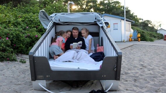 Ein Mann und drei Mädchen sitzen in einem Schlafstrandkorb. © NDR Foto: Oliver Kring