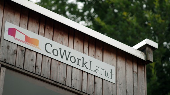 An einer Holzwand ist ein Schild angebracht auf dem "CoWorkLand" steht. © NDR 