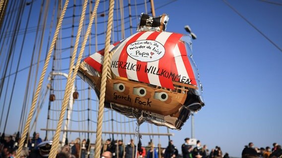 "Schön, dass du wieder da bist, Papa" steht auf einem Ballon in Form eines Piratenschiffs nach dem Anlegen des Segelschulschiffs "Gorch Fock" im Marinestützpunkt Kiel-Wik. © dpa-Bildfunk Foto: Christian Charisius