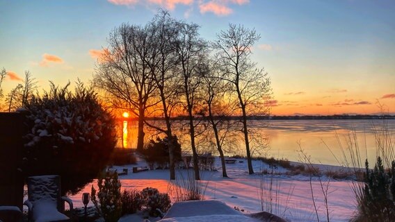 Die Sonnen geht hinter dem Wittensee unter, der Garten im Vorgergrund ist mit Schnee bedeckt. © Ulrike Maihöfer Foto: Ulrike Maihöfer