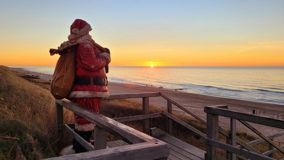 Eine Statue des Weihnachtsmann steht auf einem Strandaufgang und blickt in Richtung Sonnenuntergang. © Uwe Schmale Foto: Uwe Schmale