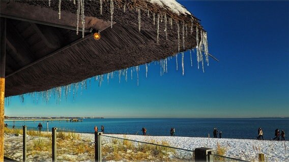 Strandansicht mit einigen spazierenden Menschen, Eiszapfen hängen von einer Hütte hinab. © Marlies Klies Foto: Marlies Klies