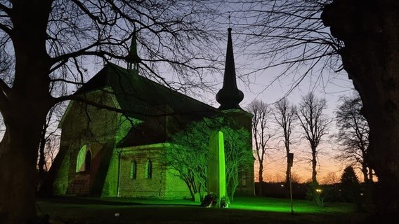 Eine grün beleuchtete Kirche steht zwischen Bäumen. © Jörg Köhnke Foto: Jörg Köhnke