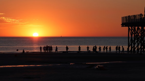 Menschen stehen am Strand von Sankt Peter-Ording und beobachten den Sonnenuntergang. © Frank Kossiski Foto: Frank Kossiski