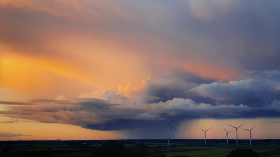 Ein Lanschaftsbild. Im Hintergrund Windräder und darüber Wolkenberge mit einem Lichtspiel am Himmel. © Britta Klein Foto: Britta Klein