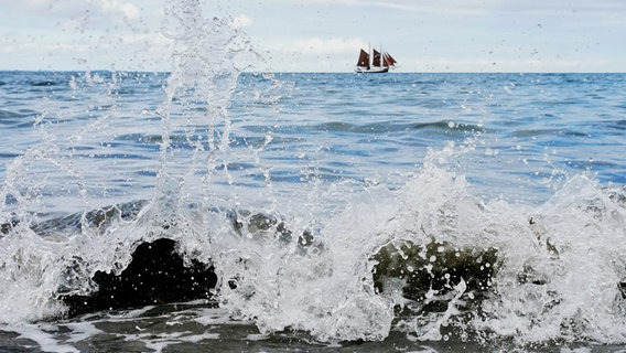 Wellen schlagen gegen Steine im Wasser, am Horizont fährt ein Segelschiff © Stefanie Rocek Foto: Stefanie Rocek