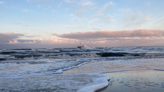 Wellen am Strand und einem kleinen Boot auf dem Meer in der Ferne. © Mareike Bohm Foto: Mareike Bohm