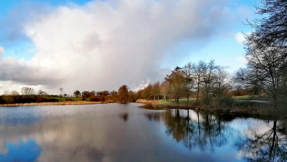 Wolken stehen über einem Teich, das Licht der Sonne spiegelt sich an der Wasseroberfläche. © Hans-Jürgen von Hemm Foto: Hans-Jürgen von Hemm