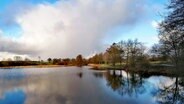 Wolken stehen über einem Teich, das Licht der Sonne spiegelt sich an der Wasseroberfläche. © Hans-Jürgen von Hemm Foto: Hans-Jürgen von Hemm